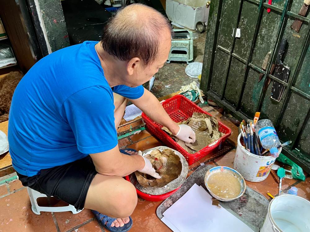 Ông Nguyễn Văn Hòa tỉ mỉ bồi từng lớp giấy vào khuôn để tạo hình mặt nạ. Đây là công đoạn quan trọng quyết định độ bền và phom dáng của sản phẩm. Ảnh: Quỳnh Mai