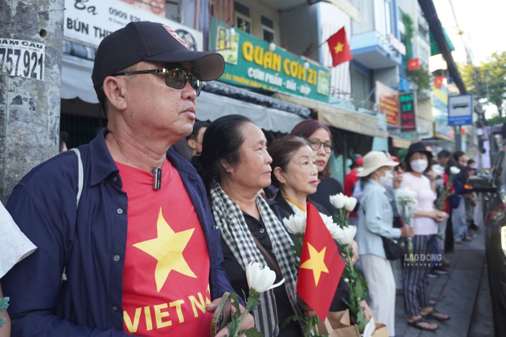 Người dân đứng trên đường Trường Sơn, trên tay mỗi người đều cầm theo một cành qua cúc trắng để trước ngực. Ảnh: Như Quỳnh